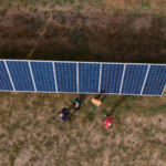 Aerial view of solar panels in a field with four adults looking up.