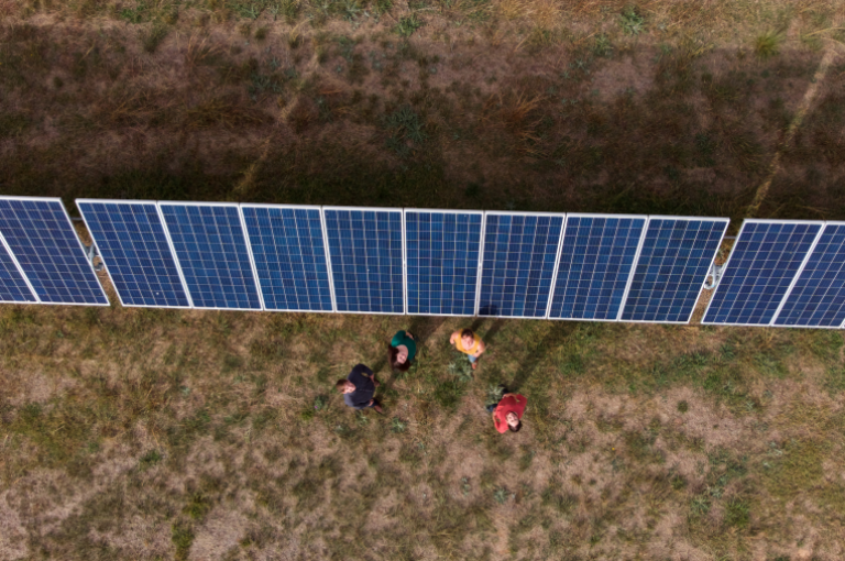 Aerial view of solar panels in a field with four adults looking up.